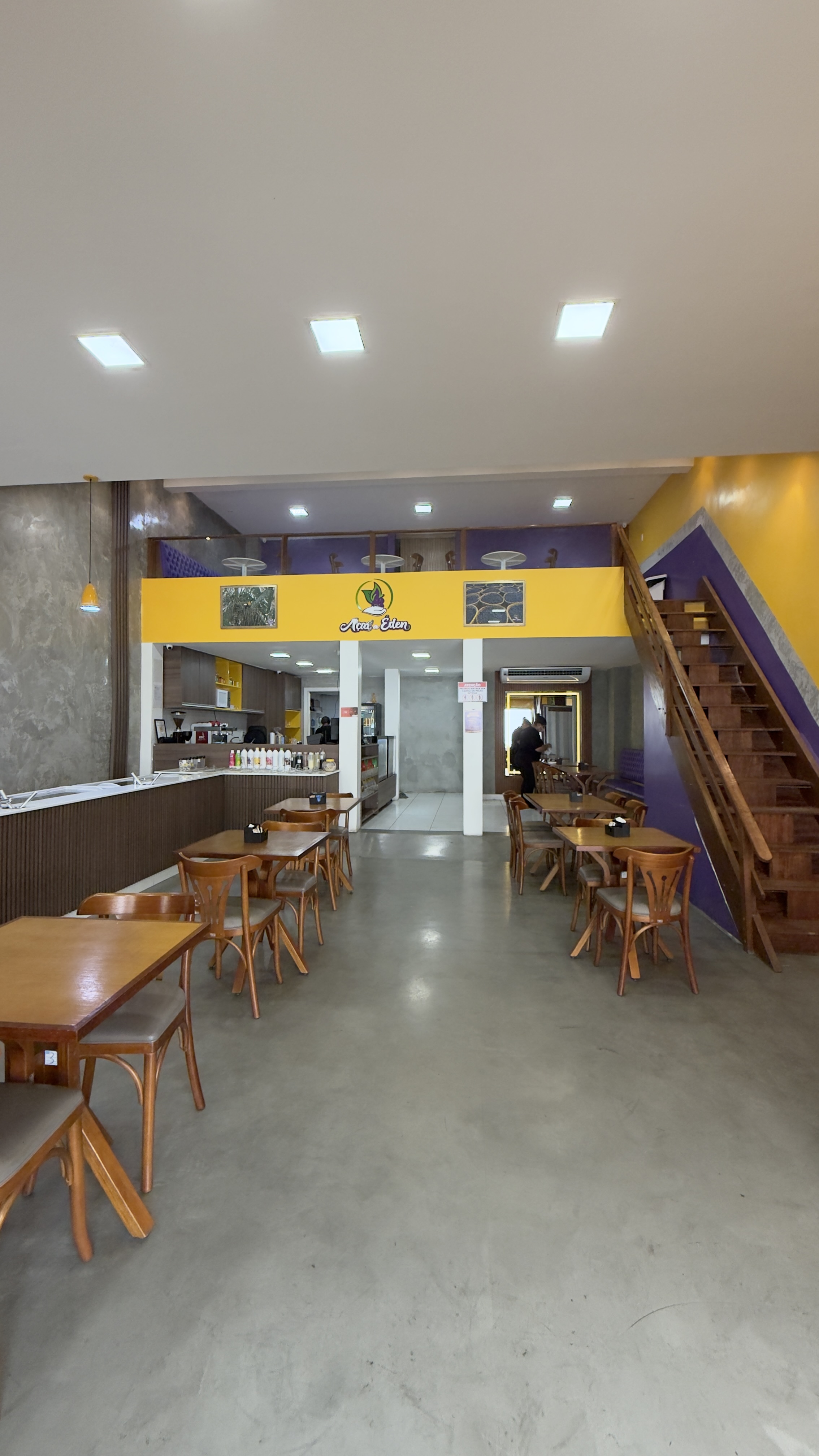 Salão interno da Açaí do Éden com mezanino, escada de madeira e parede roxa